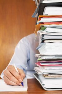 Man Writing On Notebook Next To Tall Stack Of Books